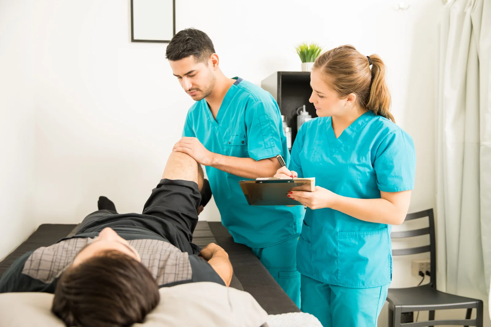 66e6a20793fbd-young-physiotherapist-examining-customer-s-leg-while-colleague-noting-clipboard-hospital-2048x1365.jpg